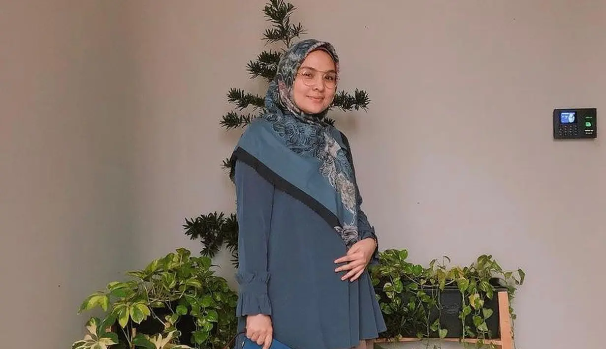 Cocok untuk outfit ke kantor, padukan tunik warna biru polos dengan rok plisket warna cokelat. Agar look makin stand out, bisa pilih hijab bermotif seperti potret ini! (Instagram/riamiranda).