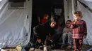 Philippe Lazzarini juga menekankan bahwa bantuan kemanusiaan yang diizinkan masuk saat ini jauh dari skala yang dibutuhkan untuk menangani krisis. Tampak dalam foto, seorang perempuan Palestina memanaskan panci sementara anak-anak memperhatikan di luar tenda tempat tinggalnya saat wilayah tersebut dilanda hujan dan kondisi musim dingin yang dingin, di Kota Gaza pada 28 Desember 2025. (Omar AL-QATTAA/AFP)
