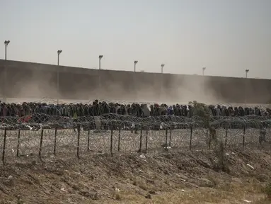 Migran berbaris antara penghalang kawat berduri dan pagar perbatasan di perbatasan AS-Meksiko, seperti yang terlihat dari Ciudad Juarez, Meksiko, Selasa (9/5/2023). (AP Photo/Christian Chavez)