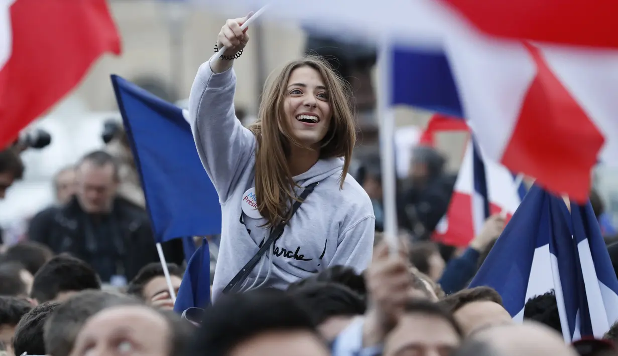 Seorang wanita mengibarkan bendera Prancis saat merayakan kemenangan Emmanuel Macron di luar museum Louvre, Paris, Minggu (7/5). Emanuel Macron akhirnya memenangi Pilpres Prancis putaran kedua, mengalahkan rivalnya Marine Le Pen. (Patrick KOVARIK / AFP)