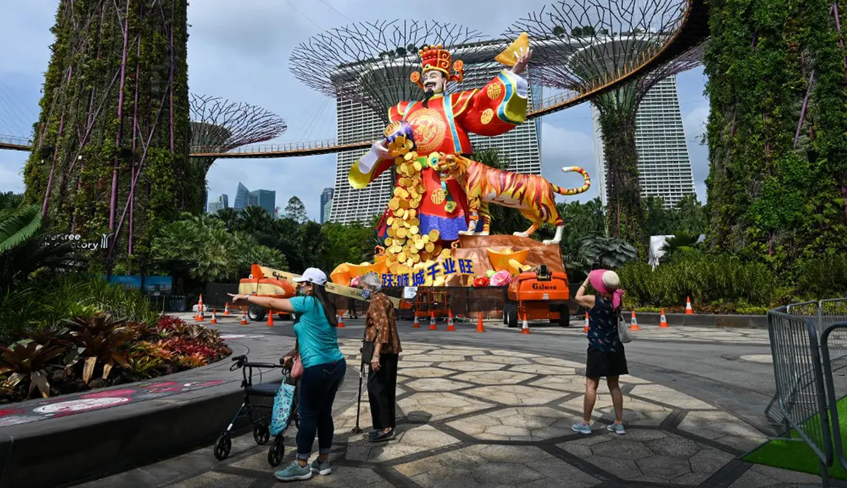 Seorang pengunjung (kanan) mengambil gambar patung lentera Dewa Keberuntungan untuk perayaan Tahun Baru Imlek mendatang di Gardens by the Bay Supertree Grove, Singapura, 18 Januari 2022. (Roslan RAHMAN/AFP)