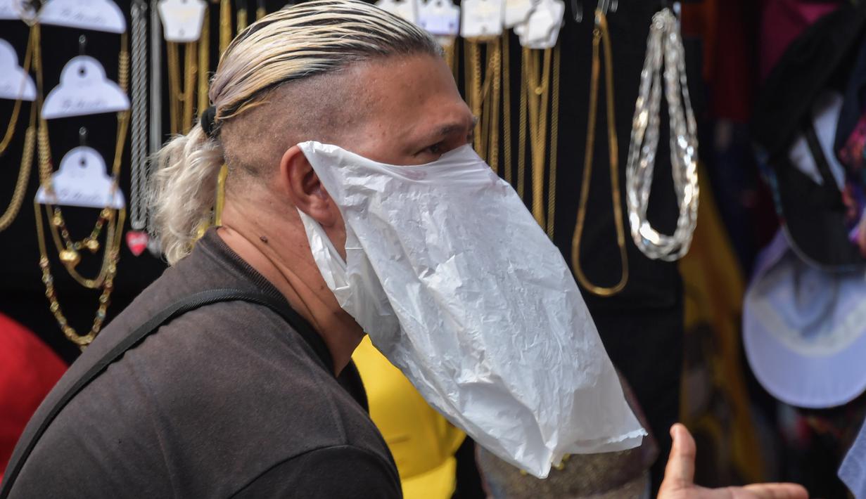 Seorang pedagang kaki lima memakai tas plastik sebagai masker di tengah pandemi virus corona baru, COVID-19, di pusat kota Sao Paulo, Brasil, pada 16 Maret 2020. Masker dijadikan masyarakat pilihan untuk mencegah penyebaran virus corona yang terus meningkat di seluruh dunia.  (NELSON ALMEIDA/AFP)