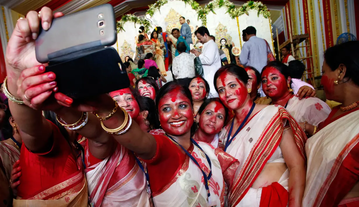 Wanita Hindu berselfie didekat patung dewi Durga pada hari terakhir festival Durga Puja di Mumbai, India (11/10). Festival ini semakin populer pada masa Kemaharajaan Britania di Bengali. (AP Photo/Rajanish Kakade)