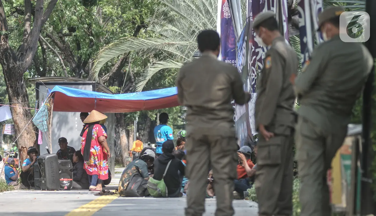 Petugas Satpol PP berjaga saat warga gusuran Kampung Bayam menggelar aksi di depan Balai Kota, Jakarta, Senin (5/12/2022). Nasib warga Kampung Bayam di kawasan Jakarta International Stadium (JIS), Jakarta Utara, kian merana. Meski sudah diresmikan Gubernur DKI Jakarta Anies Baswedan pada 12 Oktober 2022,  sampai saat ini mereka belum bisa menghuni gedung empat lantai tersebut. (merdeka.com/Iqbal S. Nugroho)