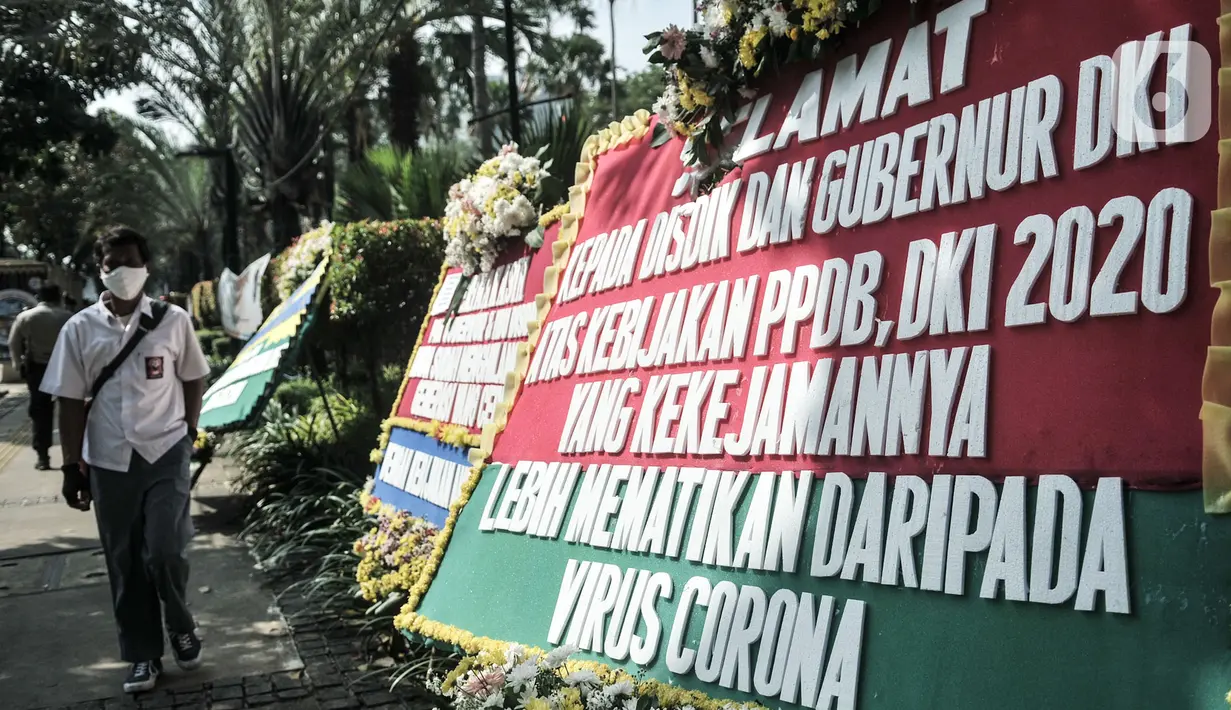 Massa dari Relawan PPDB DKI Jakarta 2020 melintas di depan karangan bunga yang terpajang di Balai Kota DKI Jakarta, Senin (6/7/2020). Karangan bunga itu bentuk kekecewaan terhadap Gubernur Anies Baswedan dan Kadisdik DKI terkait penerimaan siswa baru Jalur Zonasi. (merdeka.com/Iqbal Nugroho)