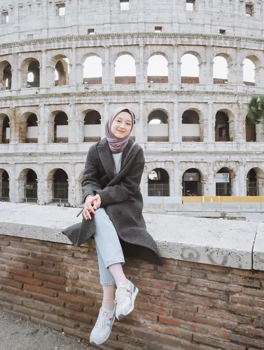 Berlibur ke Colosseum di Roma, Italia, Gita mengenakan coat berwarna abu-abu yang dipadukan dengan hijab segiempat berwarna taro, celana jeans, dan sneakers. (Liputan6.com/IG/@gitasav)