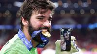 Kiper Liverpool, Alisson, menggigit medali usai menjuarai Liga Champions 2019 di Stadion Wanda Metropolitano, Madrid, Minggu (2/6). Liverpool menang 2-0 atas Tottenham Hotspur. (AP/Manu Fernandez)