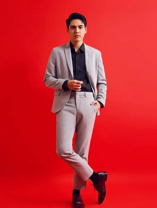 Pesona Maxime Bouttier tak perlu disangsikan lagi. Salah satu foto menampilkannya mengenakan kemeja hitam lengan panjang berbalut setelan jas abu-abu. Kaus kaki hitam dan sepatu pantofel hitam bertali menyempurnakan penampilannya. Auranya makin memancar berkat latar merah polos. Terasa kontras sekaligus menajamkan derajat ketampanan. (Foto: Dok. Instagram @bouttier_maxime)
