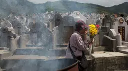 Seorang wanita membawa bunga selama festival Qingming di pemakaman di Hong Kong (5/4). Festival Qingming atau dikenal sebagai Hari Pembersihan Makam untuk menghormati orang yang dicintainya yang telah tiada. (AFP Photo/Isaac Lawrence)