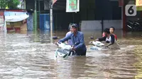 Warga membawa motor melintasi banjir yang merendam jalan Raya KH Hasyim Ashari, Ciledug ,Tangerang, Rabu (1/1/2020). Banjir setinggi dada orang dewasa membuat jalur penghubung Tangerang ke Jakarta tersebut terputus tidak dapat dilintasi. (Liputan6.com/Angga Yuniar)