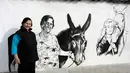 Sabka (82) melintasi dinding yang dilukis mural bergambar Putri Diana, di desa Staro Zhelezare, Bulgaria, Kamis (27/7). Penduduk setempat memenuhi dinding bagian luar rumah mereka dengan mural sejumlah tokoh dan musisi dunia. (AP Photo/Valentina Petrova)