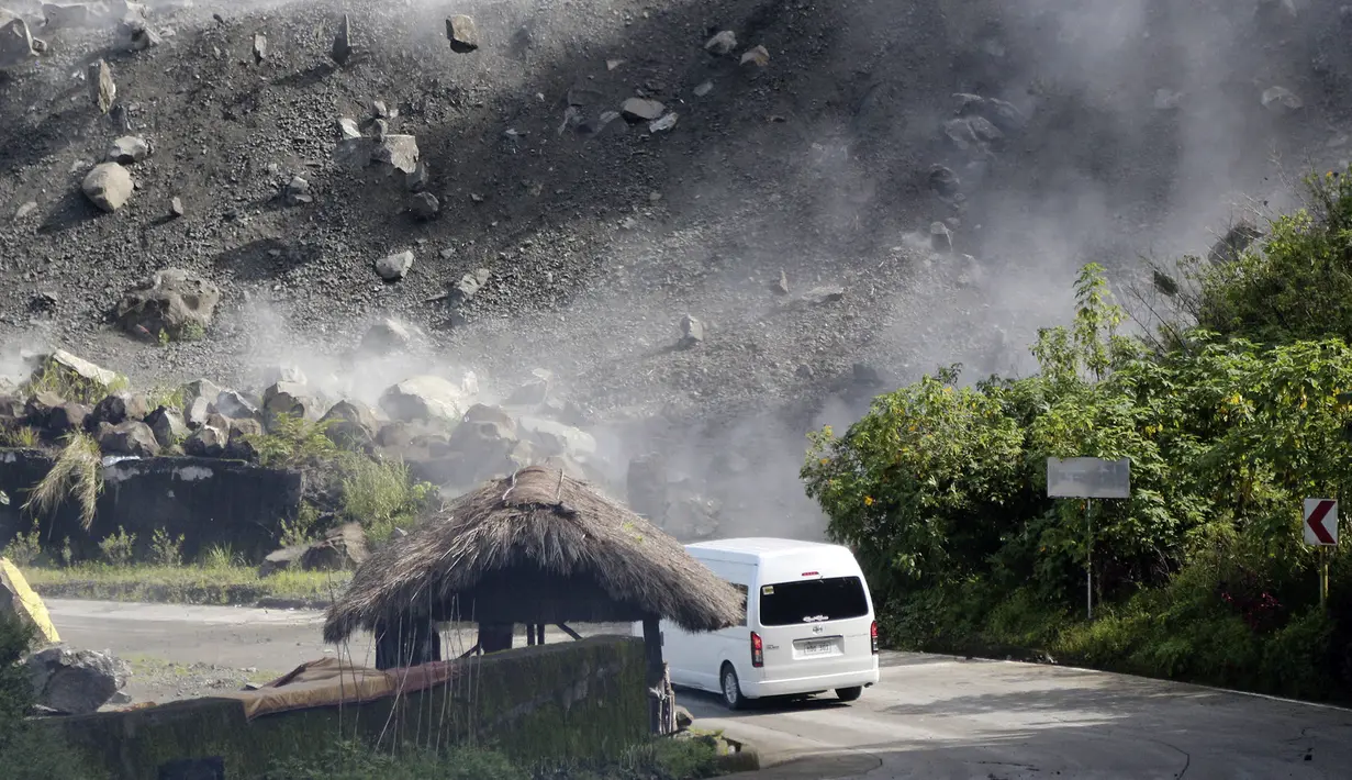 Batu-batu besar berjatuhan saat kendaraan melewati jalan selama gempa bumi di Bauko, Provinsi Mountain, Filipina, 27 Juli 2022. Gempa bumi kuat memicu tanah longsor dan merusak bangunan di Filipina. (AP Photo/Harley Palangchao)