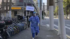 Pekerja dengan alat pelindung memegang tanda bertuliskan "Jangan berkerumun" selama hari pengujian massal bagi penduduk di distrik Jingan, Shanghai barat (4/4/2022). China telah mengirim lebih dari 10.000 petugas kesehatan ke Shanghai, termasuk 2.000 staf medis militer. (AP Photo/Chen Si)