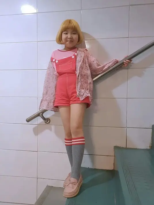 Dengan rambut pirangnya, Go Do Yoen tampil staylish bergaya layering mengenakan overall pendek pink dikombinasika  dengan tshirt sebagai inner dan jaket bermotif. Untuk melengkapi penampilannya, ia memilih sepatu dengan kaos kaki panjang abu-abu. Instagramnya @lee_6038.