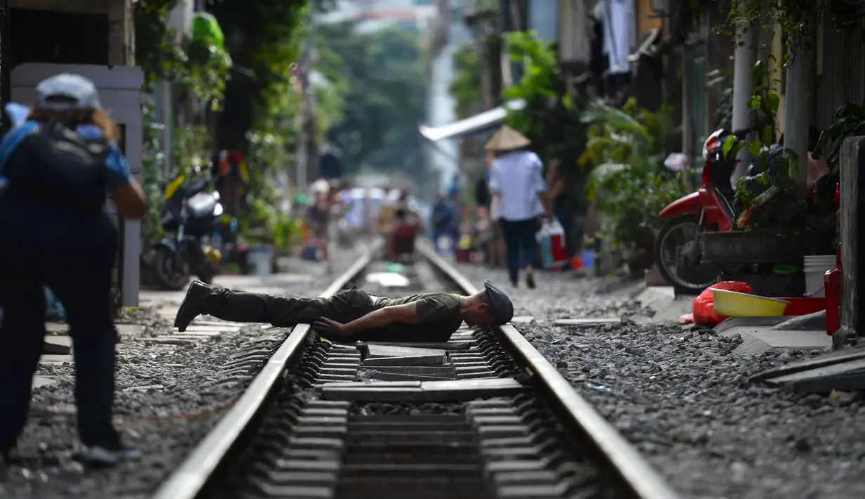 Gambar pada 15 Oktober 2018, turis berpose untuk foto di tengah jalur kereta api yang melintasi kawasan permukiman di Hanoi, Vietnam. Beberapa tahun terakhir, pengunjung ke kawasan ini lebih menyukai mengambil kesempatan untuk fotografi. (Nhac NGUYEN/AFP)