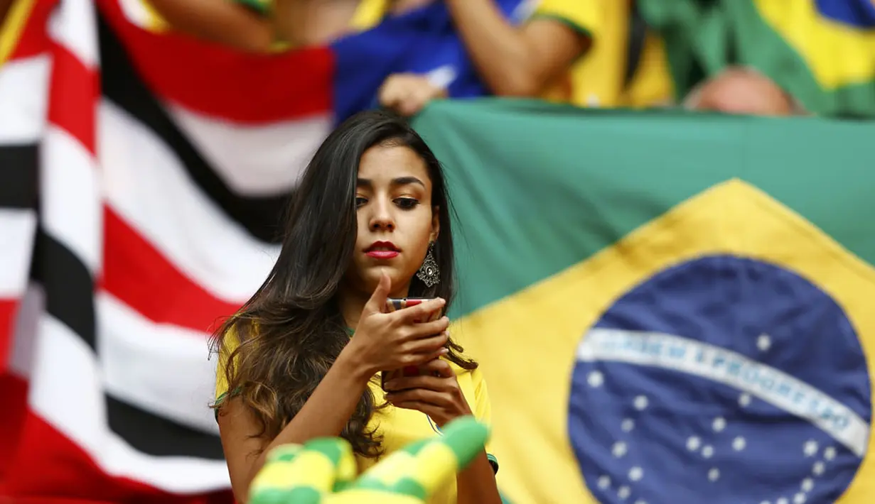 Sambil menunggu dimulainya laga Kamerun vs Brasil di Stadion Nasional Brasil, (23/6/2014), salah satu suporter Selecao terlihat memainkan ponselnya. (REUTERS/Dominic Ebenbichler)
