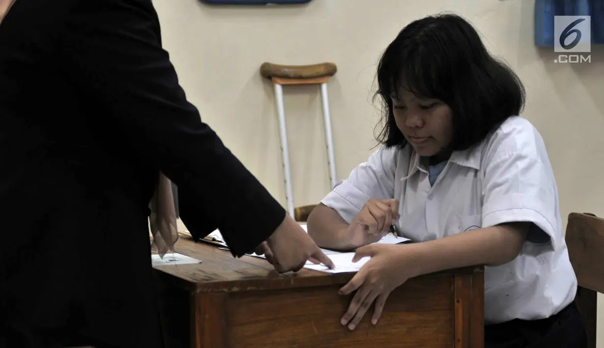 Guru pengawas saat membimbing siswa mengisi biodata pada lembar jawaban UNKP di SLB Negeri 7 Jakarta, Selasa (24/4). Seluruh siswa yang mengikuti ujian tersebut merupakan penyandang tunarungu. (Merdeka.com/Iqbal Nugroho)