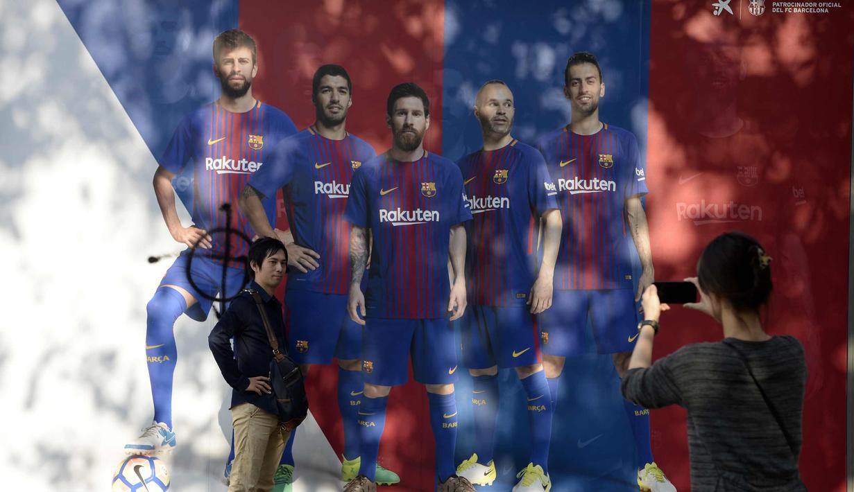 Fans berpose di dekat poster Gerard Pique yang dirusak di sebuah toko di luar stadion Camp Nou, Barcelona (3/10). Akibatnya Pique terancam dicoret dari segala kegiatan yang dilakoni La Furia Roja, julukan Timnas Spanyol. (AFP Photo/Josep Lago)