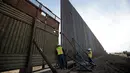 Pekerja melihat di antara pagar perbatasan Amerika Serikat (AS) dengan Meksiko di Calexico, California, AS, Minggu (5/3). Pembangunan tembok pembatas di area ini sudah direncanakan sejak zaman Barack Obama tahun 2009. (AP Photo/Gregory Bull)