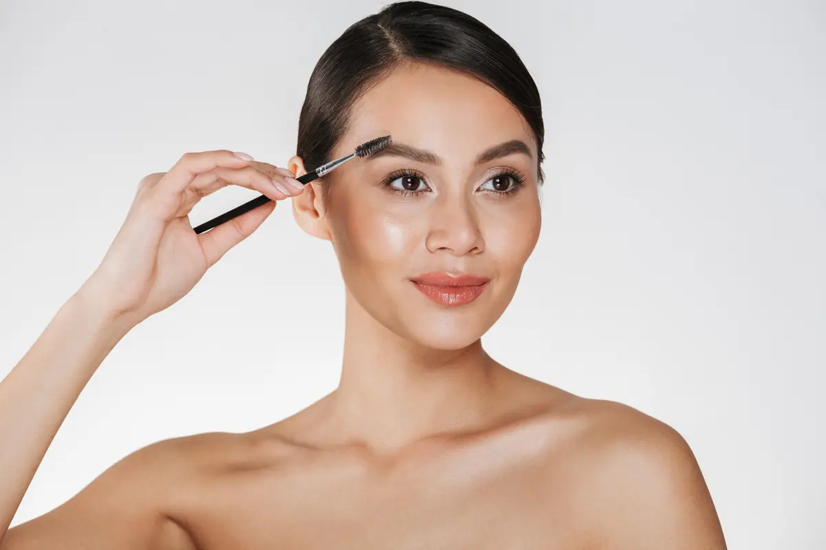 Seorang perempuan sedang merapikan alisnya menggunakan brush make up (Foto Dok: Freepik/ drobotdean)