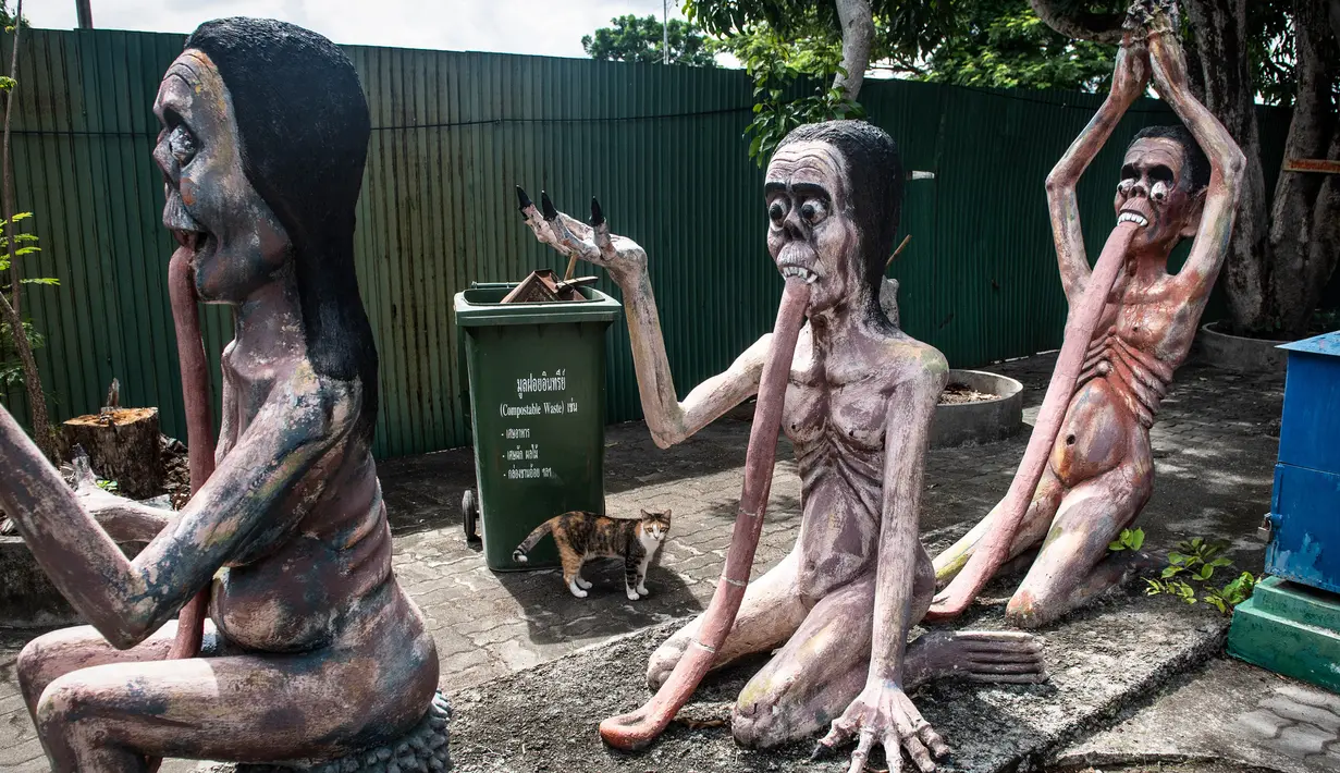 Seekor kucing berjalan melewati patung-patung yang menggambarkan nasib orang-orang yang melakukan perbuatan buruk di taman yang menggambarkan neraka versi Buddha di kuil Wat Saeng Suk di provinsi pantai Thailand Chonburi (9/7/2020). (AFP/Lillian Suwanrumpha)