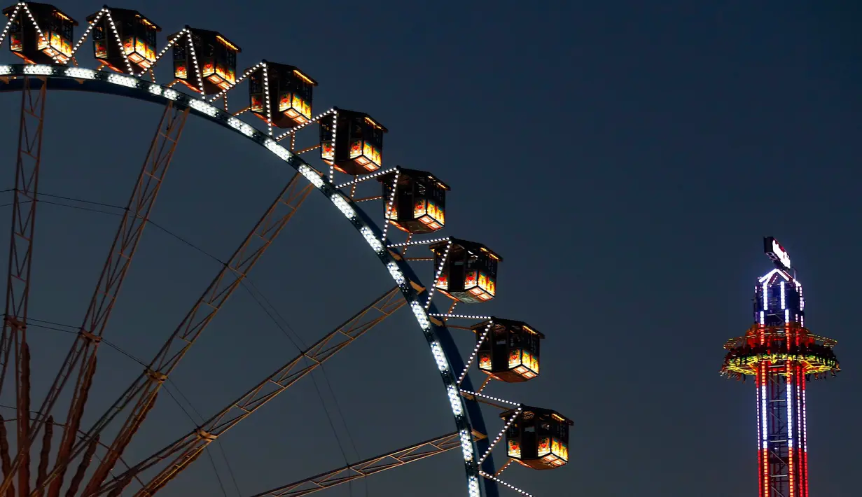 Pengunjung menikmati wahana taman hiburan di belakang kincir raksasa saat festival Oktoberfest di Munich, 27 September 2018. Oktoberfest adalah rangkaian festival terbesar di dunia yang diadakan setiap tahun oleh masyarakat Jerman. (AP/Matthias Schrader)