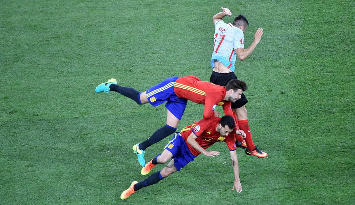 Pemain Spanyol, Gerard Pique dan Sergio Busquets, terjatih saat bereut bola dengan pemain Turki, Burak Yilmaz, pada laga Grup D Piala Eropa 2016 di Allianz Riviera, Nice, Sabtu (18/6/2016) dini hari WIB. (AFP/Bertrand Langlois)