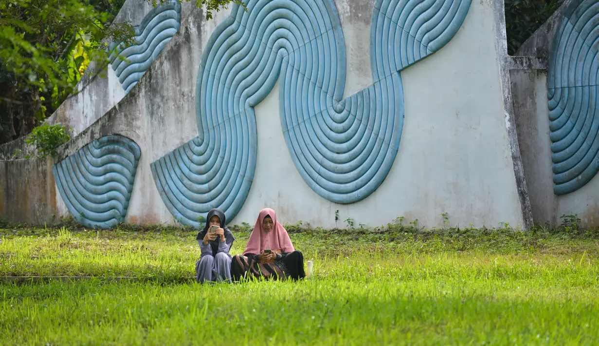Seorang perempuan dan anaknya berdoa saat memperingati 18 tahun musibah gempa dan tsunami di kuburan massal Siron, Aceh, Senin (26/12/2022). Tsunami Aceh pada 2004 merenggut nyawa lebih dari 170.000 orang di Indonesia saja. (AFP/Chaideer Mahyuddin)
