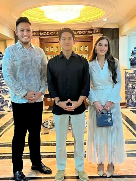 Anisha Rosnah tampil serba putih dengan atasan blazer dipadukan rok panjang plisket sambil membawa mini bag warna biru. [@support.anishaik]