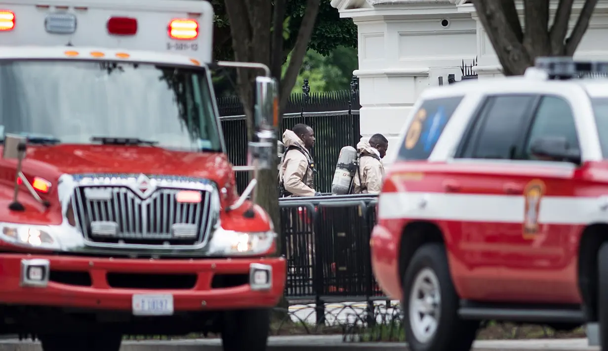 Petugas darurat dengan baju pelindung berjalan menuju gerbang bagian utara Gedung Putih, Washington, DC, Senin (30/5). Gedung Putih ditutup sebagian untuk menyelidiki sebuah benda mencurigakan yang dilemparkan melalui pagar. (Brendan Smialowski/AFP)