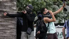 Demonstran berselfie ketika yang lain menggunakan ketapel menyerang polisi selama bentrok memprotes kebijakan ekonomi pemerintah di Santiago (6/11/2019). Presiden Chile mengatakan "tidak menyembunyikan apa-apa" mengenai tuduhan bahwa polisi membunuh, menyiksa warga sipil. (AFP Photo/Javier Torres)