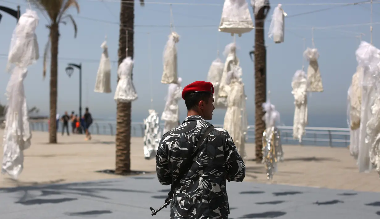 Seorang petugas keamanan berjaga dekat puluhan gaun pengantin yang digantung di tepi pantai Beirut, Sabtu (22/4). Gaun yang digantung di tepi pantai itu sebagai bentuk protes Undang-Undang Pemerkosaan di Lebanon oleh sekelompok aktivis. (PATRICK BAZ/AFP)