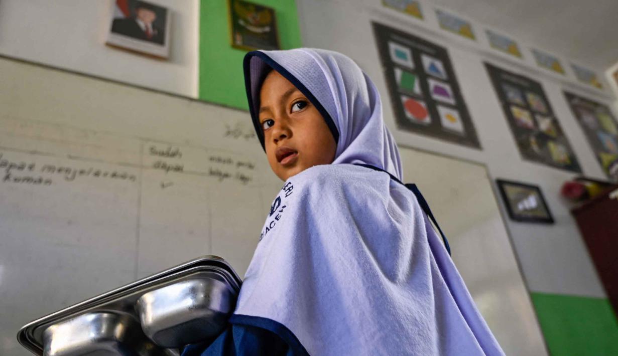Seorang siswa membawa nampan berisi makanan yang dipasok oleh program Makan Bergizi Gratis (MBG) di sebuah sekolah dasar di Banda Aceh pada Kamis 30 Oktober 2025. Program ini menyasar peserta didik dari jenjang PAUD hingga SMA/sederajat. (CHAIDEER MAHYUDDIN/AFP)