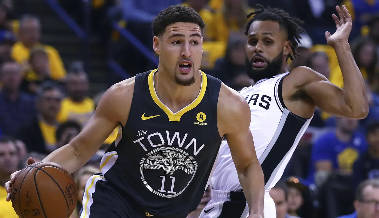 Aksi pemain Warriors, Klay Thompson (kiri) menggigiring bola melewati adangan pemain Spurs, Patty Mills pada game kedua putaran pertama playoffs NBA Basketball di Oracle Arena, Oakland, California, (16/4/2018). Warriors menang 116-101. (AP/Ben Margot)