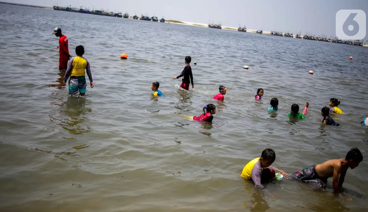 Anak-anak berenang saat petugas (kiri) mencari ubur-ubur di Pantai Lagoon, Ancol Taman Impian, Jakarta, Rabu (9/10/2019). Pihak Ancol telah memasang jaring agar ubur-ubur itu tidak sampai ke tempat warga yang sedang berenang. (Liputan6.com/Faizal Fanani)