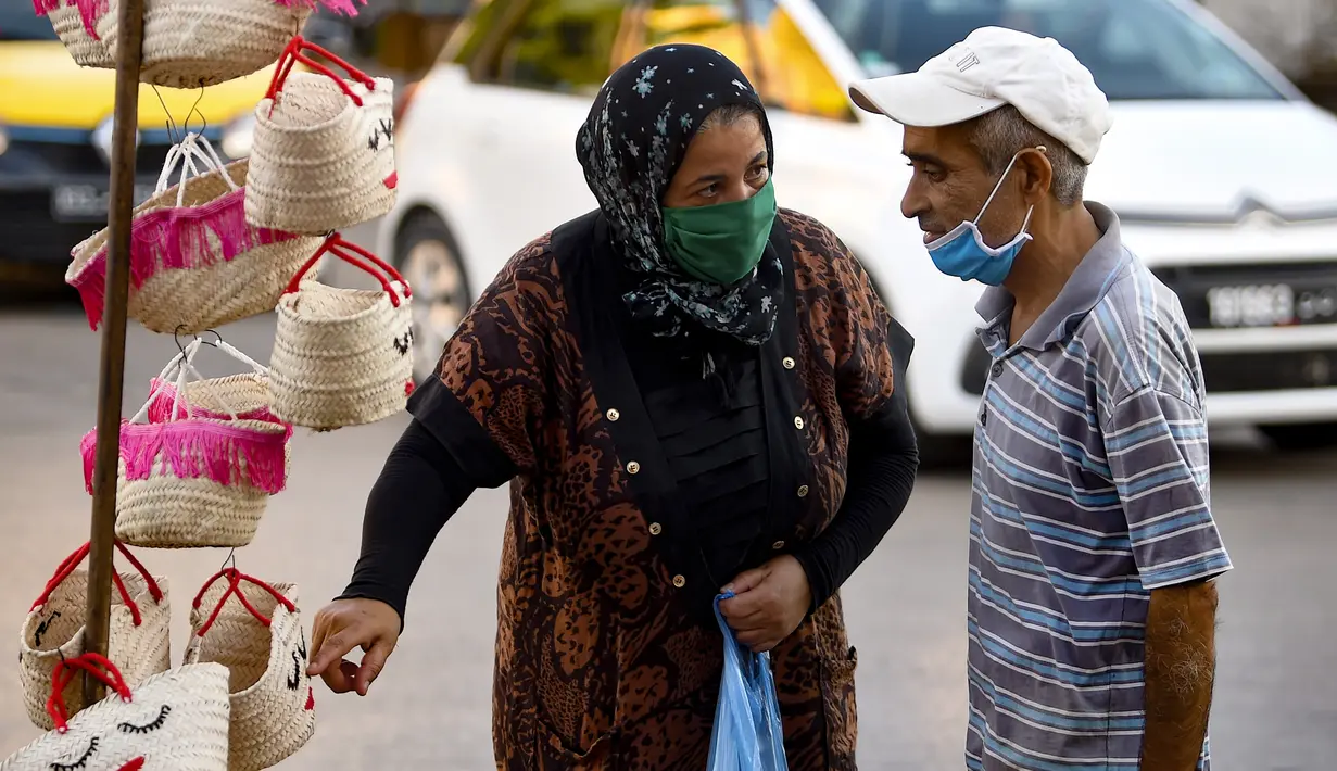Perempuan Tunisia yang mengenakan masker berbincang dengan seorang penjual di sebuah pasar ketika kasus baru infeksi Corona melonjak, di kota Gabes, Rabu (27/8/2020). Tunisia pada 25 Agustus 2020 melaporkan peningkatan tertinggi kasus baru Covid-19 dibandingkan minggu sebelumnya. (FETHI BELAID/AFP)