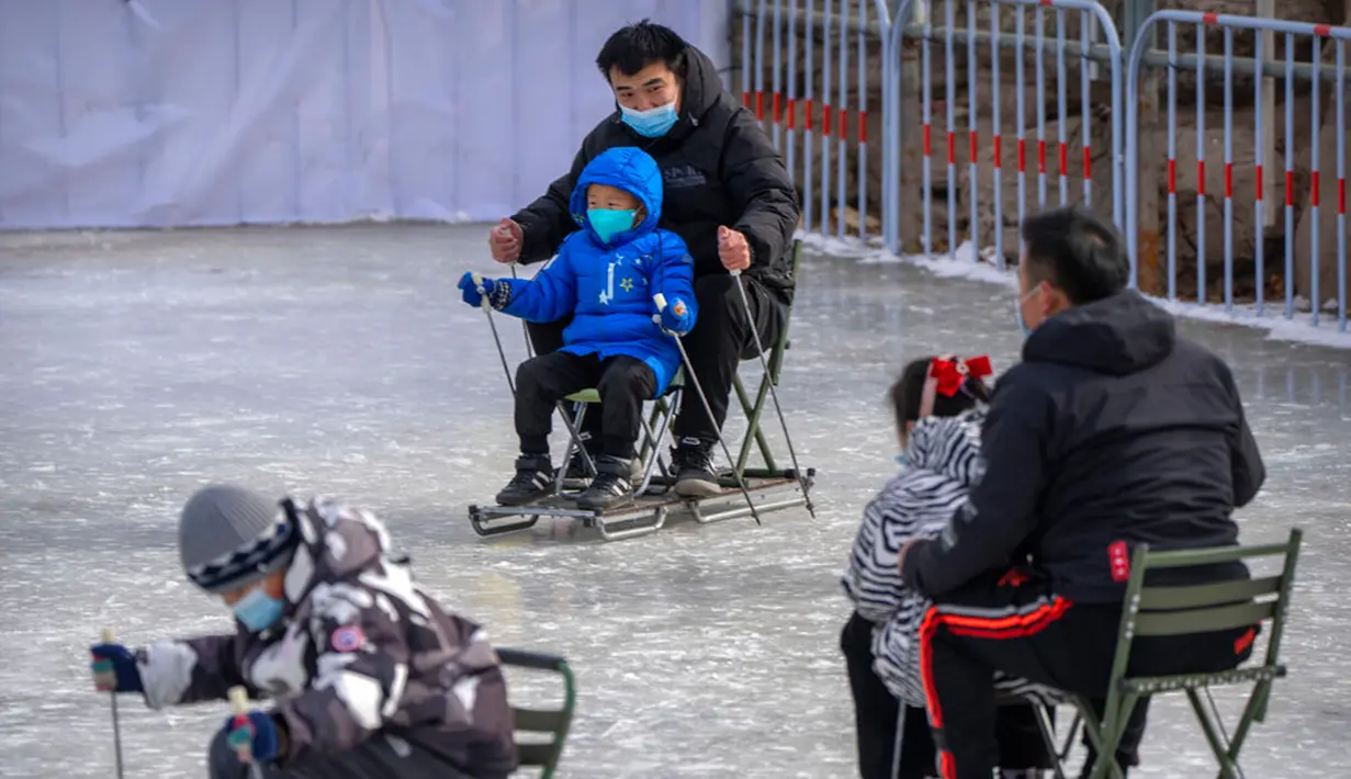Seorang pria dan anak-anak menggunakan kursi yang dimodifikasi untuk meluncur melintasi es dalam kolam di taman umum saat pekan liburan Tahun Baru Imlek di Beijing, China, Kamis (26/1/2023). (AP Photo/Mark Schiefelbein)