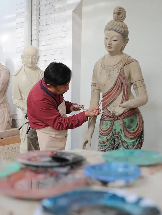 Seniman Du Yongwei mewarnai sebuah patung dengan cat di Dunhuang, Provinsi Gansu, China, Minggu (5/4/2020). Du Yongwei (60) sudah menggeluti seni mewarnai patung selama lebih dari 40 tahun. (Xinhua/Du Zheyu)