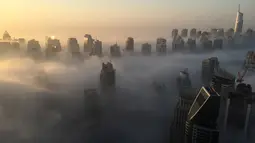 Suasana saat kabut pagi hari menyelimuti gedung-gedung pencakar langit di Kota Dubai, Uni Emirat Arab, Senin (5/12). Ketika udara dingin pada malam hari bertemu dengan pagi yang panas dan lembab, kabut terbentuk pada dini hari. (AFP/Rene Slama)