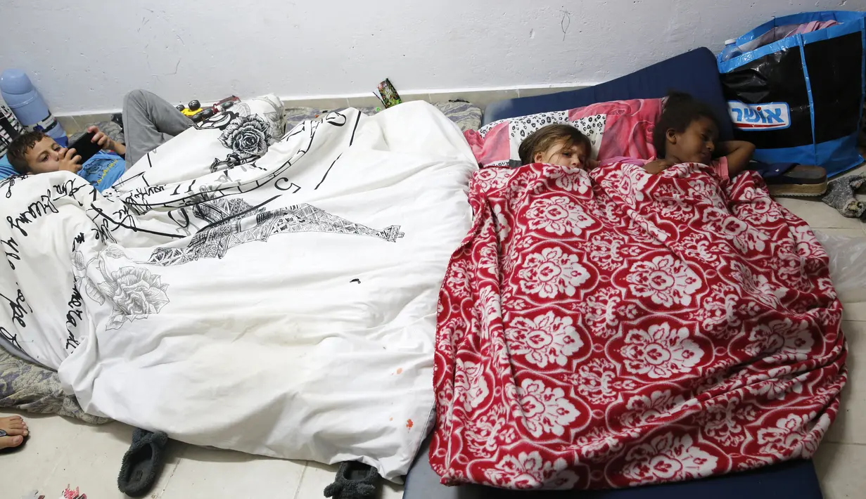 Anak-anak bersiap untuk tidur saat berlindung dari serangan roket di shelter bom Kota Ashkelon, Israel, Rabu (13/11/2019). Militan Palestina menghujani Israel dengan roket sebagai balasan atas tewasnya komandan Jihad Islam Palestina Baha Abu Al-Ata dalam serangan udara Israel. (GIL COHEN-MAGEN/AFP)