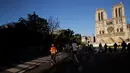Warga berolahraga di depan Katedral Notre-Dame yang kembali membunyikan lonceng utamanya di Paris, Rabu (15/4/2020). Lonceng utama katedral kembali dibunyikan setelah satu tahun mengalami kebakaran yang sampai mengejutkan seluruh warga dunia. (AP/Christophe Ena)