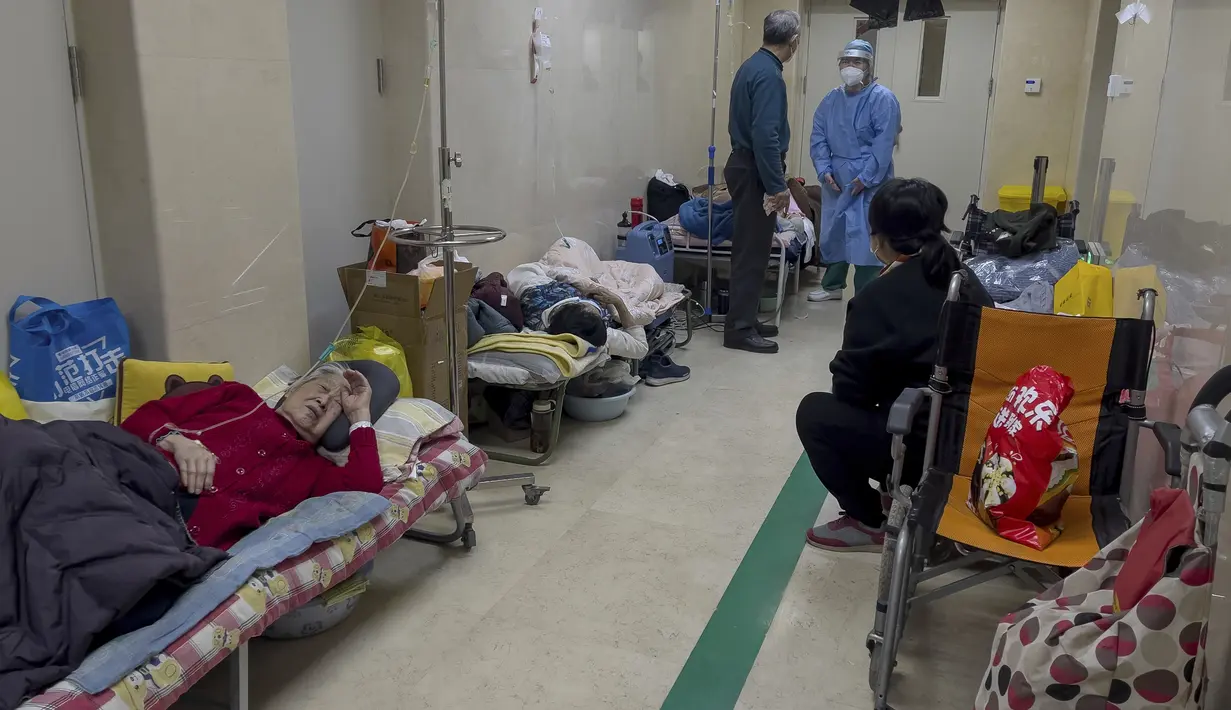 Seorang pria berbicara dengan pekerja medis ketika pasien lanjut usia beristirahat di sepanjang koridor bangsal darurat untuk menerima infus di sebuah rumah sakit di Beijing, Kamis (5/1/2023). Pasien, kebanyakan dari mereka lansia, berbaring di tandu di lorong dan menerima oksigen sambil duduk di kursi roda saat kasus COVID-19 melonjak di ibu kota China, Beijing. (AP Photo/Andy Wong)