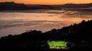 <p>Lapangan sepak bola yang berada di kawasan Mont de Gourze, Swiss barat. Keindahan suasana di sekitar lapangan semakin menjunjang berkat lampu sorot yang di latari dengan danau Jenewa yang begitu memukau. (AFP/Fabrice Coffrini)</p>