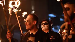 Peserta melakukan pawai sambil membawa obor dalam perayaan Bonfire Night melintasi jalan di Sussex Timur, Inggris, Selasa (5/11/2019). Obor yang mereka bawa itu nantinya akan digunakan untuk menyalakan kembang api dan api unggun. (Ben STANSALL/AFP)