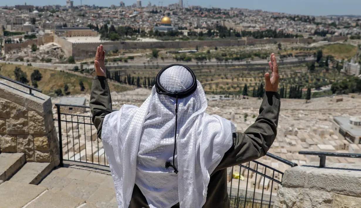 Seorang pria Palestina melaksanakan salat Jumat saat bulan Ramadan di depan Bukit Zaitun dengan latar belakang kota tua Yerusalem dan Masjid Al-Aqsa yang ditutup, Jumat (8/5/2020). Masjid Al-Aqsa telah ditutup sejak bulan lalu untuk mencegah penyebaran Covid-19. (Photo by AHMAD GHARABLI / AFP)