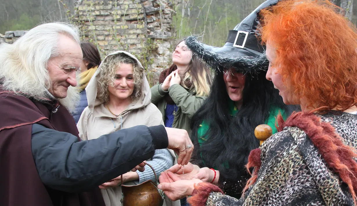 Seorang pria memberikan air kepada peserta yang hadir di acara Walpurgis Night atau Witches Night di Vilnius, Lithuania, Senin (1/5). Orang-orang yang hadir mengenakan atribut layaknya para penyihir. (AFP PHOTO / Petras Malukas)