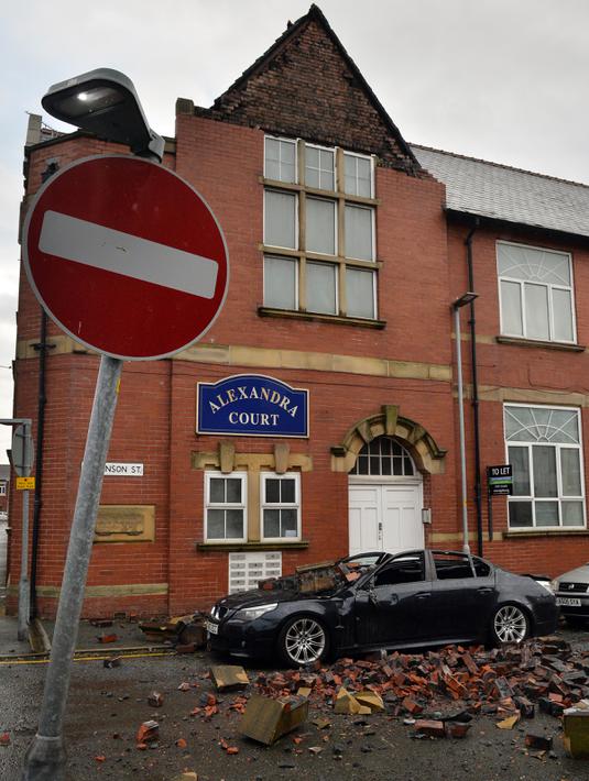 Sebuah mobil yang diparkir rusak terkena batu karena angin kencang yang disebabkan oleh atap apartemen yang runtuh di Leigh, barat laut Inggris, Rabu (18/11). (AFP PHOTO/Paul Ellis)