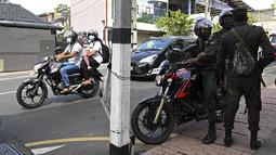 Para komuter melewati tentara yang berjaga di sepanjang jalan di Kolombo pada Sabtu (2/4/2022). Pasukan yang dipersenjatai dengan senapan serbu otomatis dikerahkan di Sri Lanka untuk mengendalikan massa, beberapa jam setelah presiden menyatakan keadaan darurat. (KODIKARA / AFP)
