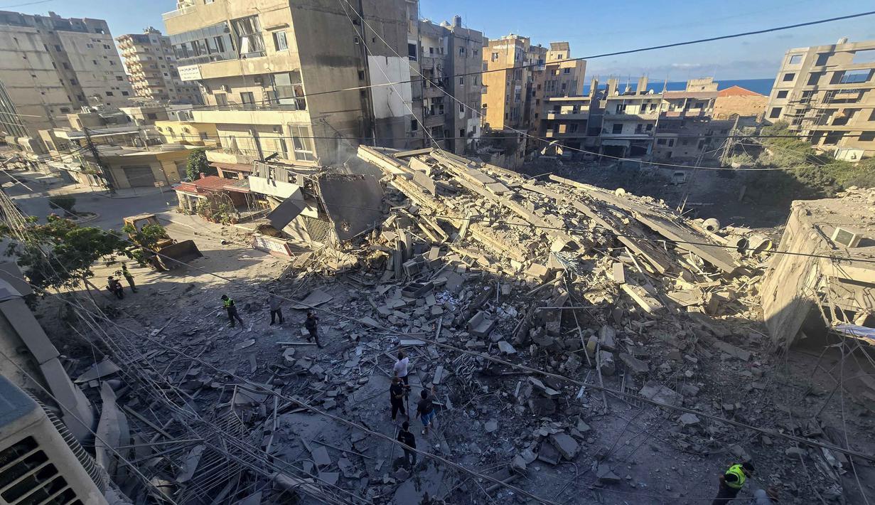 Warga menyaksikan seorang pekerja kota mengemudikan buldoser untuk membersihkan puing-puing dari jalan di lokasi serangan Israel di Tyre, Lebanon Selatan, pada Kamis 28 Mei 2026. (KAWANT HAJU/AFP)