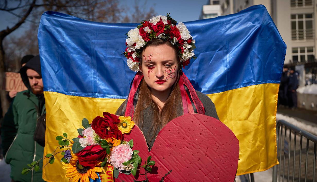 Perang mengubah arah kehidupan banyak orang. Tampak dalam foto, seorang wanita mengenakan mahkota bunga saat anggota komunitas Ukraina menggelar protes untuk menandai tahun keempat sejak dimulainya invasi skala penuh Rusia ke Ukraina di Bukares, Rumania, Minggu 22 Februari 2026. (AP Photo/Vadim Ghirda)